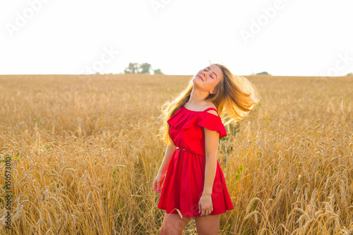 Gorgeous Romantic Girl Outdoors. Beautiful Model in Short Red Dress in Field. Long Hair Blowing in the Wind. Backlit, Warm Color Tones. © satura_