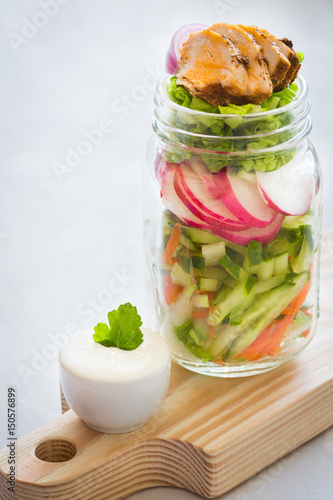 Vegetable mix and chicken slices in a glass jar yogurt sauce on wooden table. Clean eating. Healthy denner.