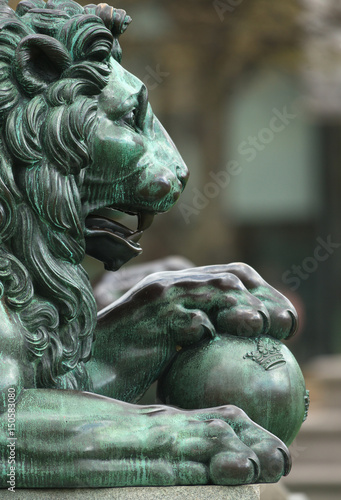 Side view of a bronze sculpture of a royal lion with the paws on a ball with the three crowns