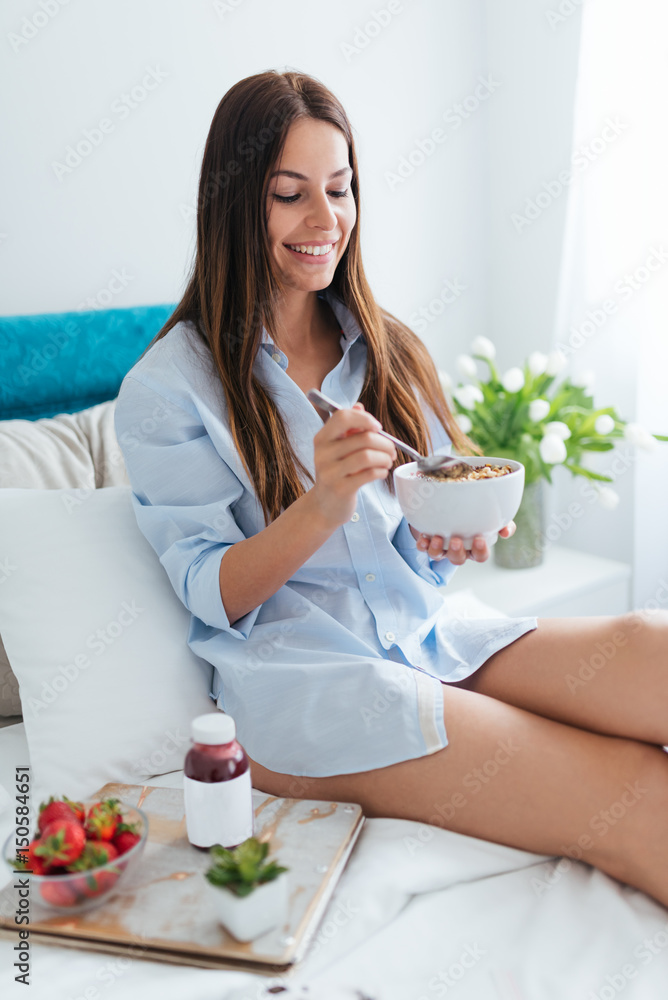 Young woman eating healthy breakfast in bed 