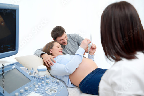 Female doctor watching her pregnant patient and her husband looking at the sonogram photo of their unborn child. Happy couple looking at the sonogram of their unborn baby copyspace pregnancy medicine.