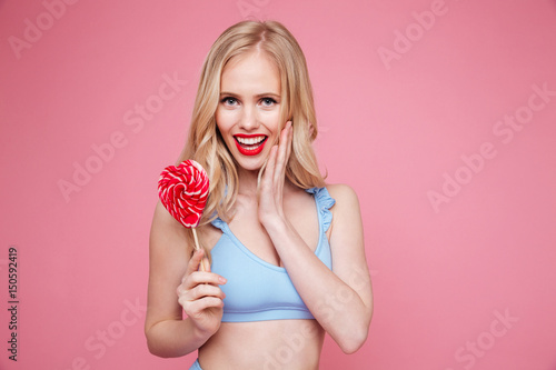 Cute blonde woman in swimsuit posing with heart shaped lollipop