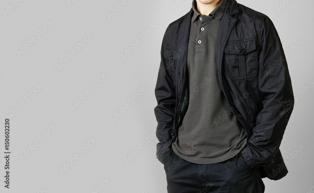 A man in a black jacket. Hands in his pockets. Isolated on grey background