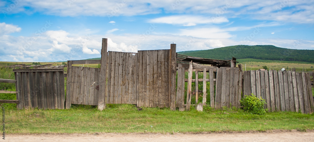 Old fence in rural areas. Green grass near an abandoned fence on the background of blue sky.