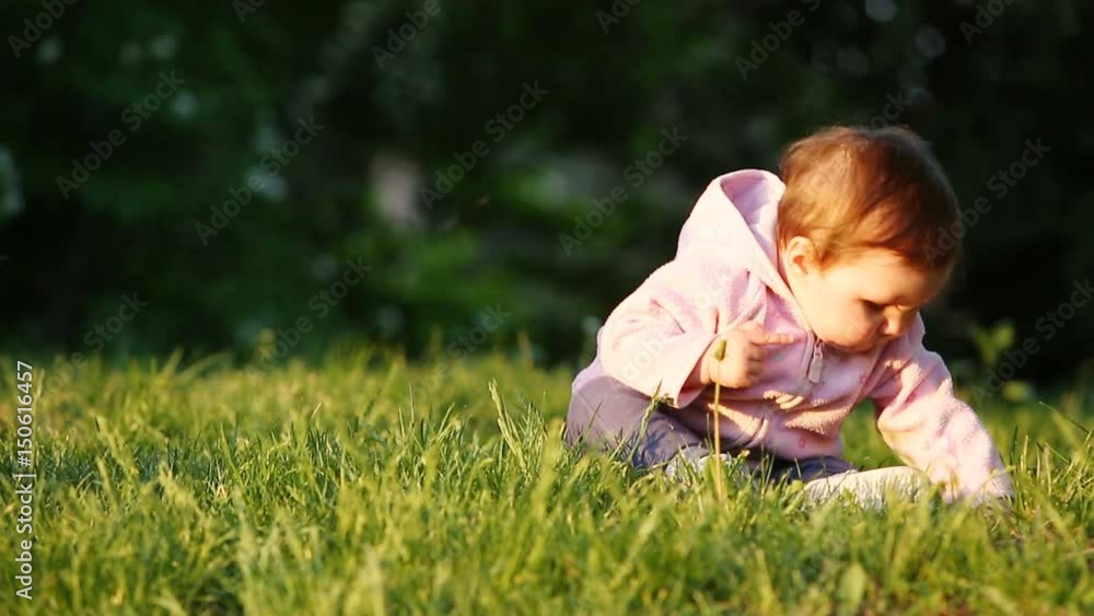 Happy little baby-girl seated on the green grass in the park at sunset. Happy little baby-girl seated on the green grass in the park at sunset.