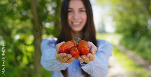 Beautiful young girl holding a twig of tomato sauce, in the background of nature. Concepts: biology, bio products, bio ecology, grow vegetables, natural clean, fresh product, vegetarians, environment.