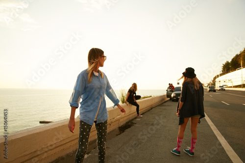 Girls travelers walking down the roadside on the sea coast on the sunset