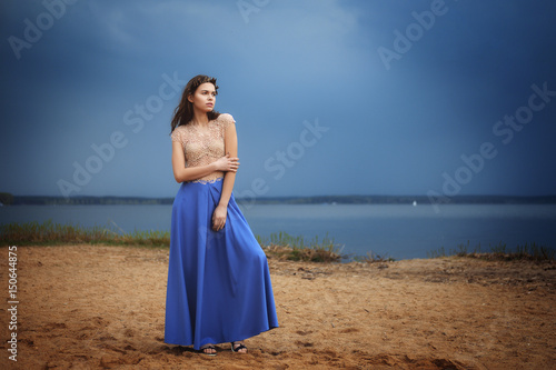 Calm lonely fashion model walking on the sand in a cloudy day. Romantic, gentle, mystical, image of a girl in long blue skirt and lace blouse. © boomeart
