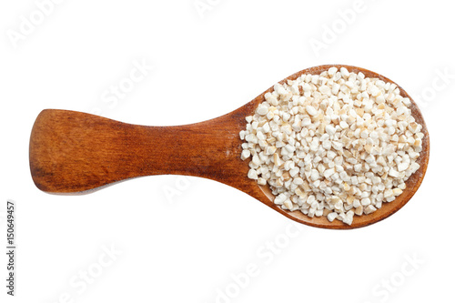 Barley groats on wooden spoon isolated on white background. Top view.