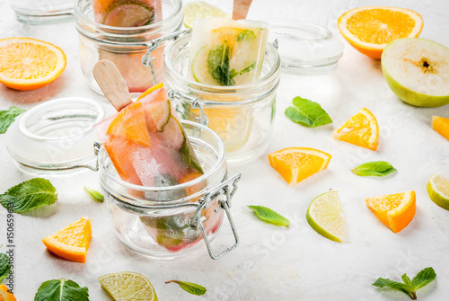 Homemade ice cream. Frozen drinks. Fresh fruits, citrus. Popsicles of red, white sangria, lemonade or mojito. With oranges, lime, mint, apples. White stone table, ingredients. Copy space