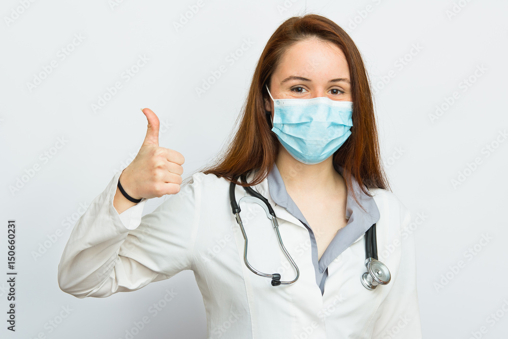 Beautiful female doctor with protecting medical mask showing thumbs up gesture on white background Beautiful female doctor with protecting medical mask showing thumbs up gesture on white background