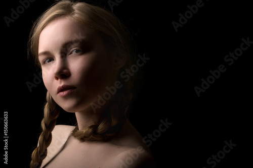 Portrait of a beautiful girl of Slavic appearance with a braid haircut on a black background.