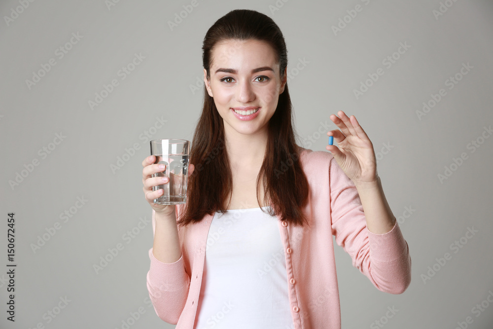 Beautiful young woman with pill and glass of water on light background Beautiful young woman with pill and glass of water on light background