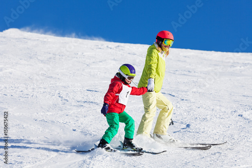 Active mother teaching son skiing holding hands