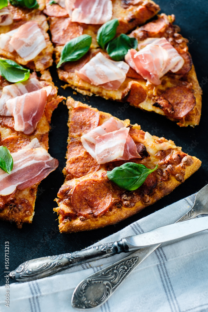 Homemade Pepperoni Pizza with fresh bacon over black background Homemade Pepperoni Pizza with fresh bacon over black background