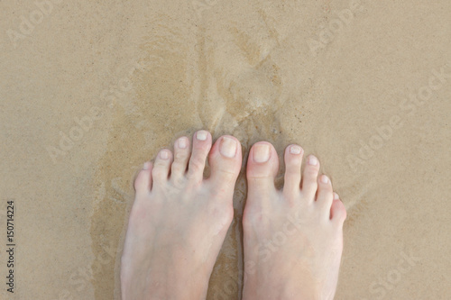 Female feet in the sand. There is a wave, and I stand and wait. Copy space. From top to bottom.