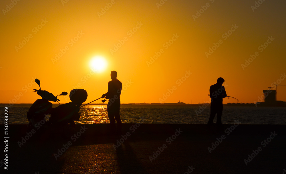 Men silhouette with fishing rod at sunset. There is a motorcycle silhouette near the man. 