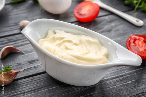 Mayonnaise in gravy boat with ingredients on wooden background, closeup