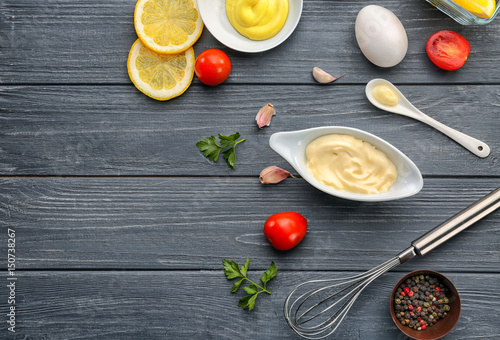 Mayonnaise in gravy boat with ingredients on wooden background, top view