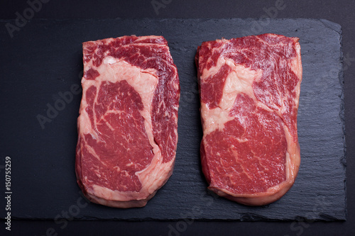 Two fresh raw marble meat, black Angus ribeye steak on a dark stone background