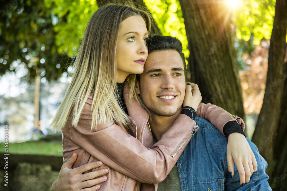 Boyfriend and girlfriend standing in countryside in green luscious field, embracing each other and cuddling, showing romantic love