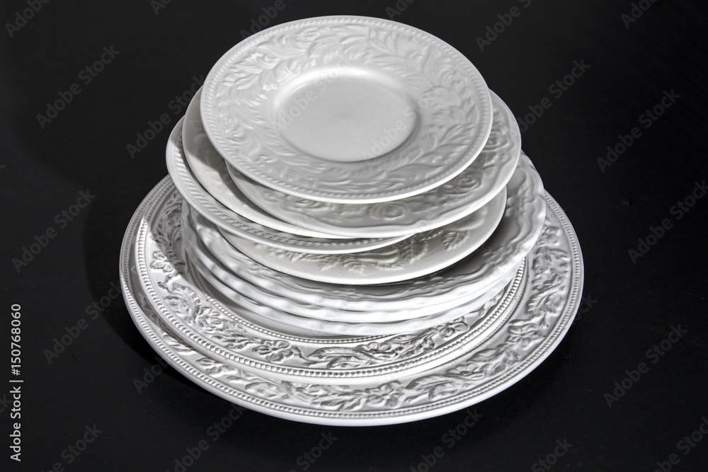 Set of white ceramic dinner relief plates on black background Set of white ceramic dinner relief plates on black background