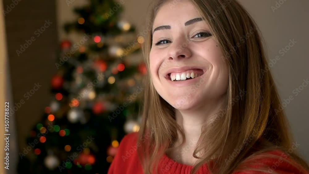 Young woman in stylish sweater posing and smiling on camera on christmas tree background. Young woman in stylish sweater posing and smiling on camera on christmas tree background.