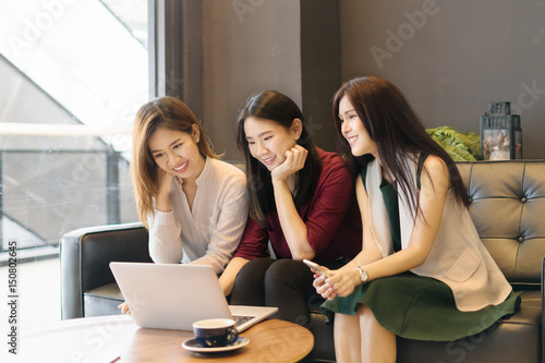 Three beautiful Asian girls using smartphone and laptop, chatting on sofa at cafe, modern lifestyle with gadget technology or working woman on casual business meeting outside office concept.