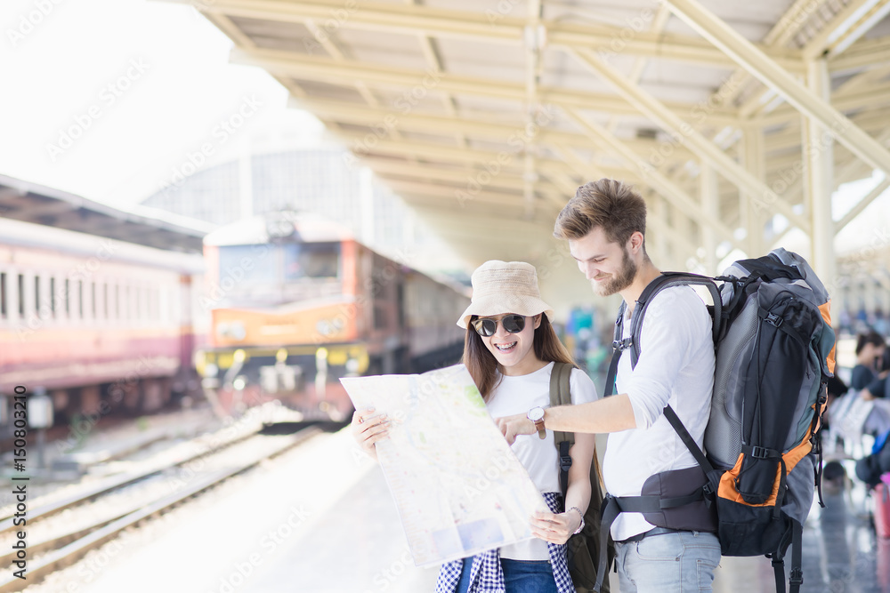 Young couple asian woman and concasian man traveler are looking the map with train station background. Travel in summer concept.
