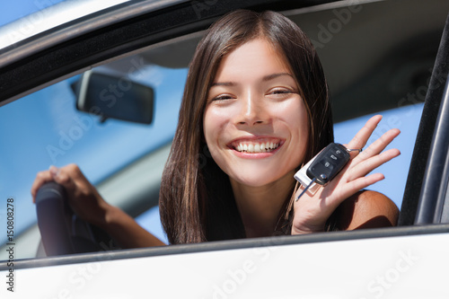 Happy Asian girl teen driver showing new car keys. Young woman smiling driving new car holding key. Interracial ethnic woman driver holding car keys driving rental car.