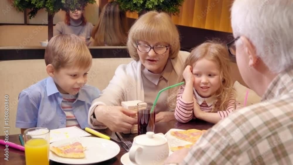Grandparents sitting at cafe table at dinner and explaining little granddaughter and grandson how to play jenga game Grandparents sitting at cafe table at dinner and explaining little granddaughter and grandson how to play jenga game