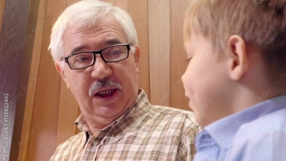 Closeup of senior man in eyeglasses having conversation with little grandson