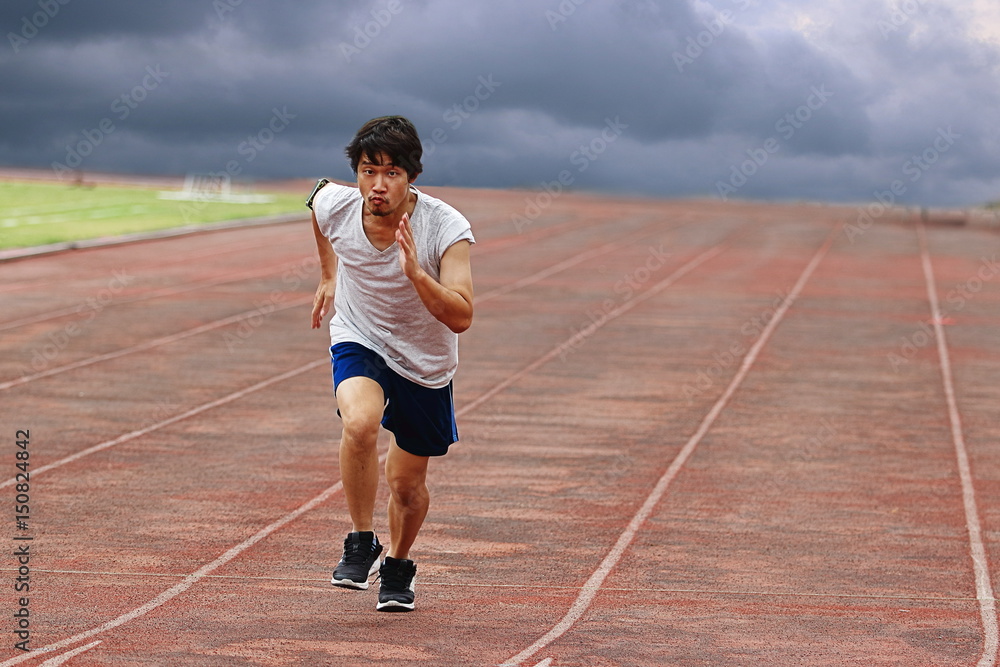 Obraz premium Young Asian runner running on track with weather storm background.