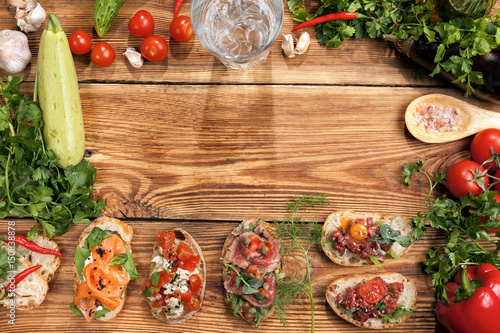 Six bruschettas with ingredients and glass of some water on a wooden table