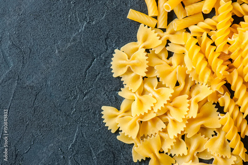 Variety of types of Italian pasta background. Set of raw pasta on a black slate background.