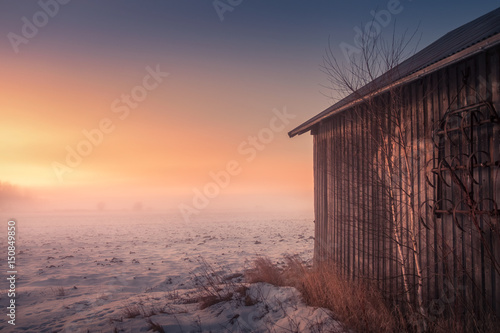 Foggy landscape with barn and sunset at evening