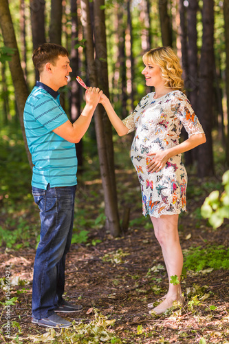 Pregnancy, family, happiness and fun concept - Man and pregnant woman have fun with candy in the park