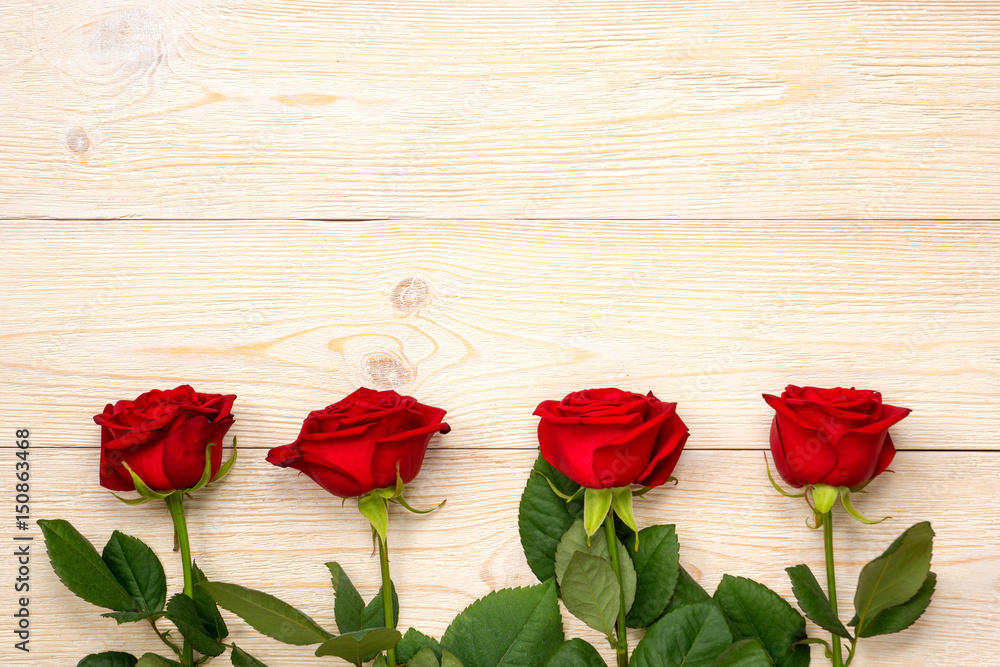 4 red roses in row over white rustic wood planks