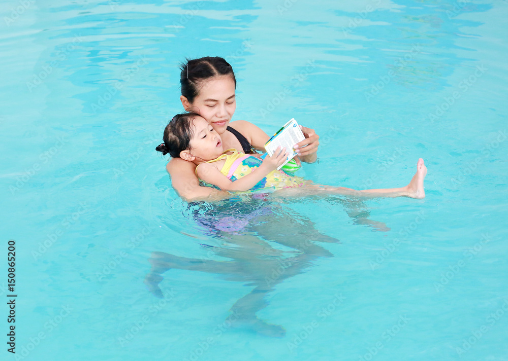 Mother and child swimming in the pool. Happy young woman teaching her daughter to swim.