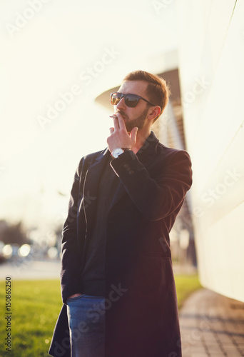 Stylish man in a coat and glasses smokes a cigarette
