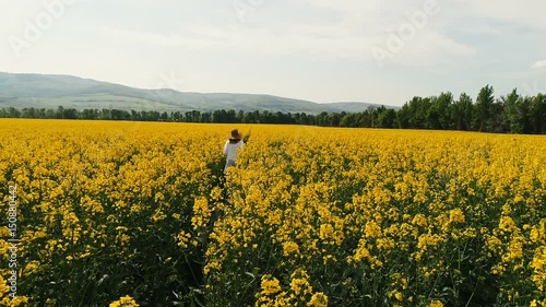 Flug mit Drohne über gelbes, blühendes Rapsfeld in dem sich eine hübsche, junge Frau befindet photo