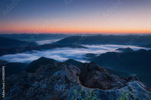 Dawn mountains landscape with fog clouds and rock on foreground.