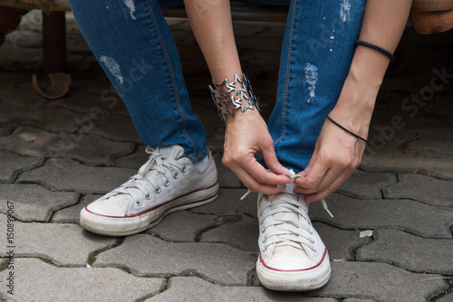 Close up female leg lacing her white sneakers and blue jean 