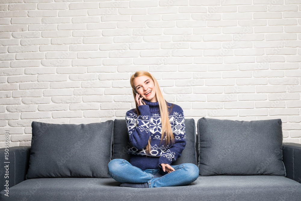 Obraz premium Beautiful young woman talking on the phone at home sitting on the couch.