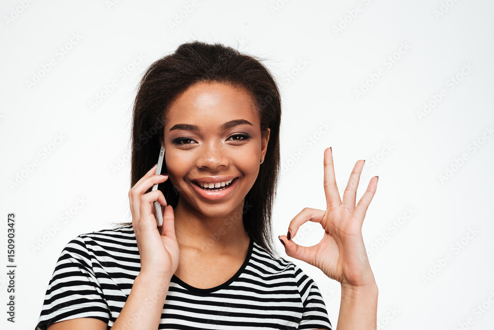 Happy young african lady talking by phone and pointing.