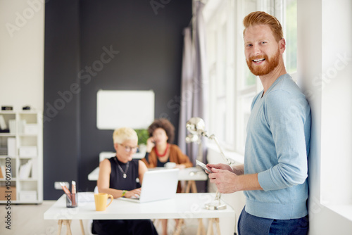 Young businessman using tablet in modern office while standing against the wall