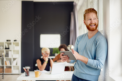 Businessman using tablet while standing in modern office and looking through window
