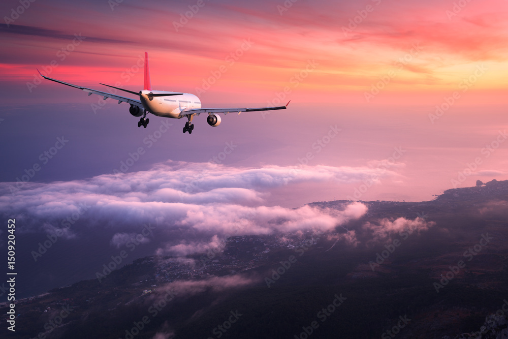 Obraz premium Airplane. Landscape with big white passenger airplane is flying in the red sky over the clouds at colorful sunset. Journey. Passenger airliner is landing at dusk. Business trip. Commercial plane