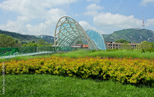 Peace of Bridge on European Square in Tbilisi, Georgia. Yellow and green spring in Tbilisi. At the right is High Mtatsminda park