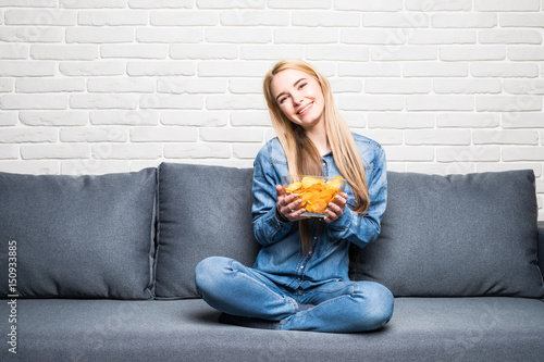 Young woman watching TV and eating chips on sofa at home